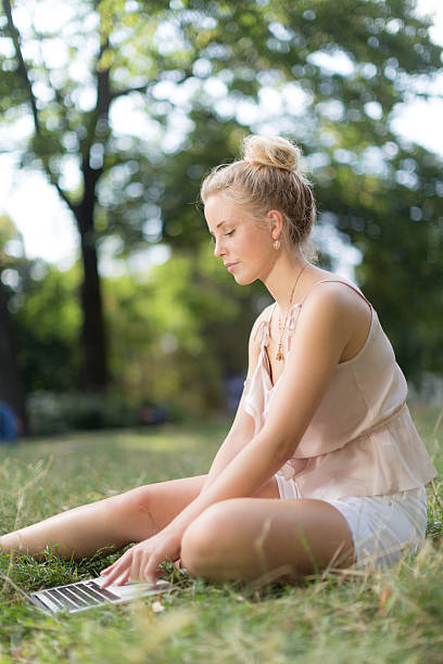 istock Young woman with computer sitting on the grass 519109283