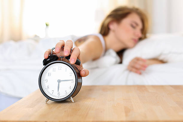 istock Sleepy young woman trying kill alarm clock 519120448