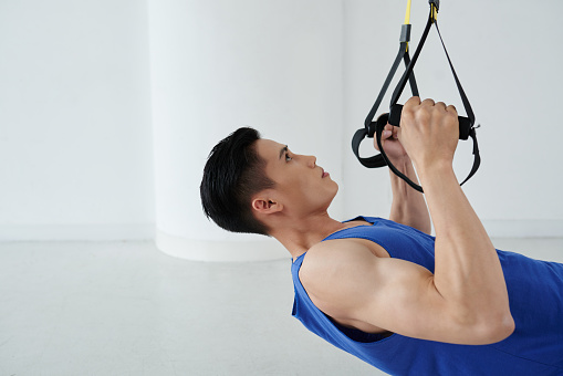 Asian young man performing trx chest exercise in the gym