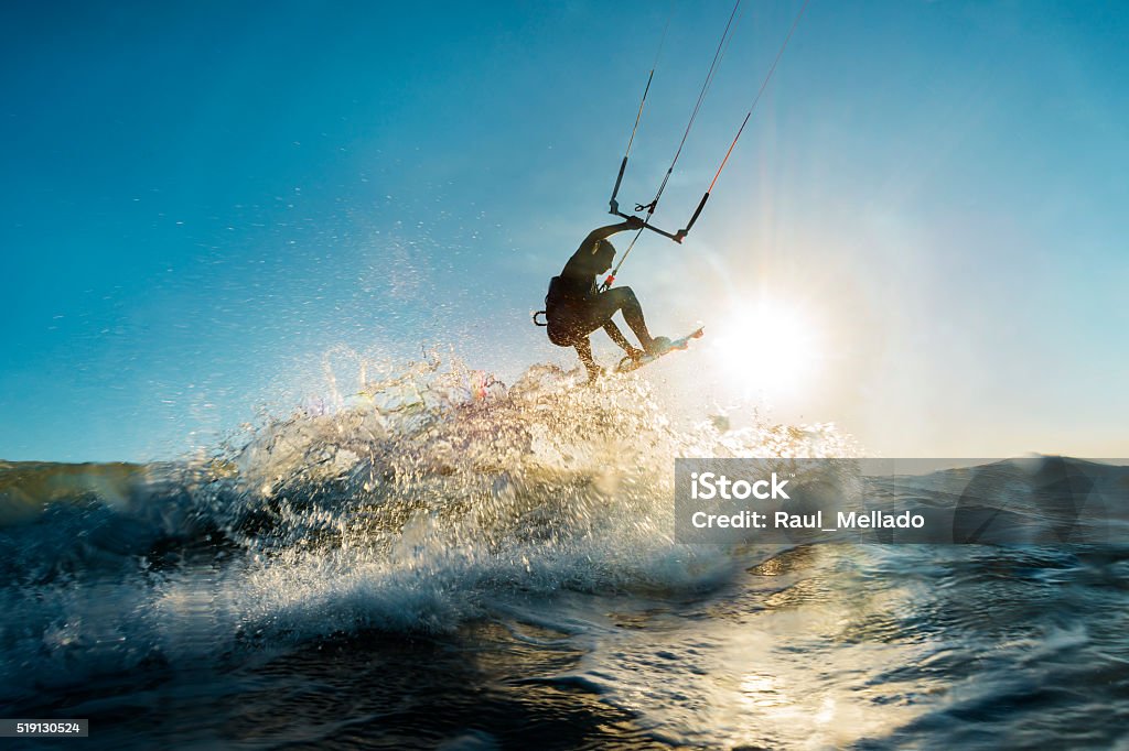 Surfer jumping at the sunset A surfer doing an amazing jump and splashing water in front of the sunset at the sea Kiteboarding Stock Photo