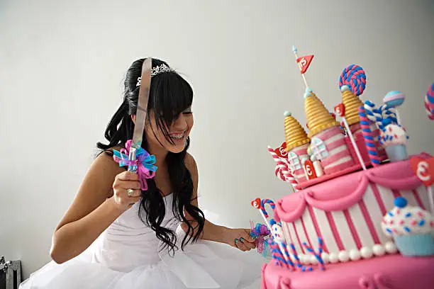 A 15 year old hispanic girl celebrates her birthday with a fancy birthday cake with a candyland theme. The three layer cake is covered with fondant and candy decorations.