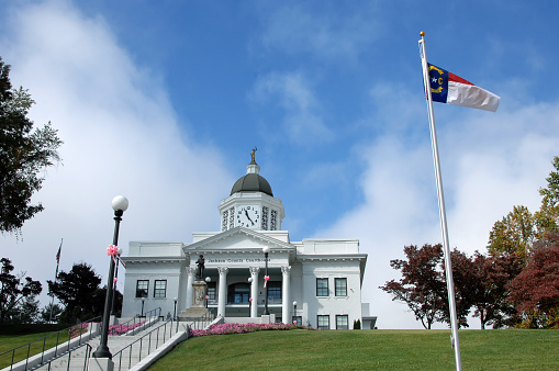Elegant Jackson County Courthouse sits on a hill overlooking the town of Sylva, North Carolina.  North Carolina flag flies against a vivid blue sky.