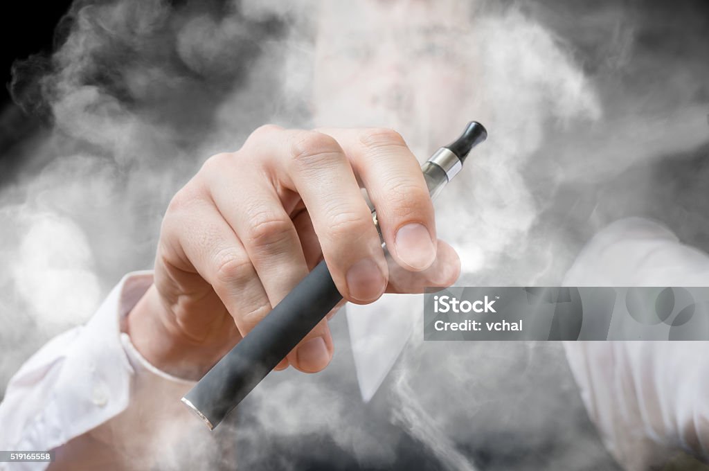 Smoking man holds electronic cigarette. A lot of smoke. Smoking man holds electronic cigarette in hand. A lot of smoke around. Cigarette Stock Photo