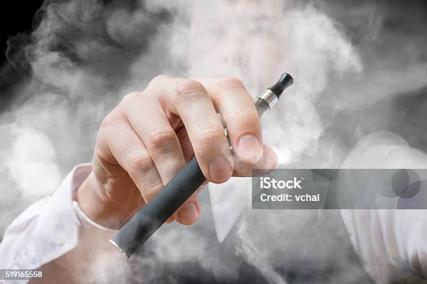 Smoking Man Holds Electronic Cigarette A Lot Of Smoke Stock Photo - Download Image Now