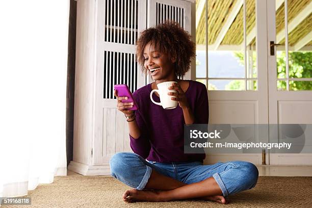 Smiling Woman Sitting On Floor At Home With Cell Phone Stock Photo - Download Image Now