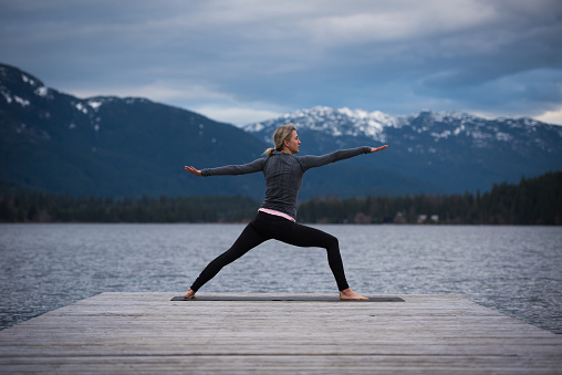 Female doing a warrior two during a yoga working at a pristine mountain lake