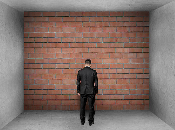 istock Businessman with bowed head stands front of a brick wall 519185786