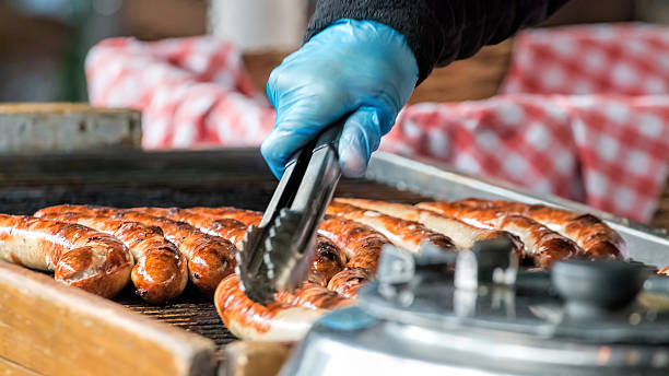 Sausages Cooking On Grill. Street Food Market Vendor Take away sausaged being grilled at public food market stand. concession stand stock pictures, royalty-free photos & images