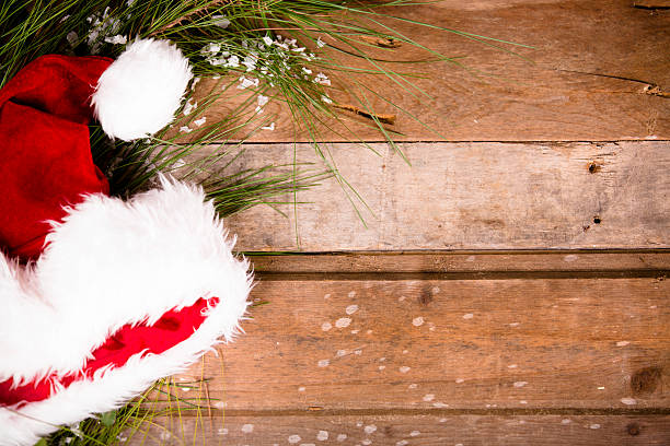 Christmas Santa hat on pine tree branch with snow. Old, rustic wooden table background. Copyspace. 