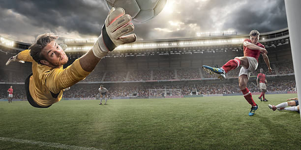 Soccer Goalkeeper A close up image of a professional soccer goalkeeper with outstretched hand reaching to make a save from rival player who has just kicked football. Action takes place in a generic floodlit outdoor stadium under a stormy evening sky. All players are wearing generic unbranded soccer kit. With intentional lensflare. scoring a goal photos stock pictures, royalty-free photos & images