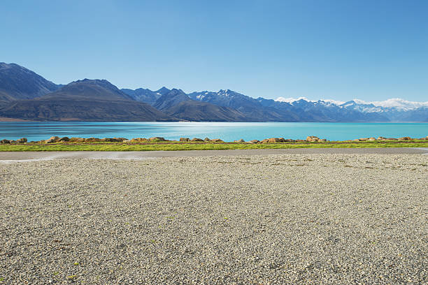 vacío rural road, cerca de lake y de montaña con nieve - gravel fotografías e imágenes de stock