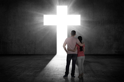 Young couple looking the shining cross on the wall. Religious concept