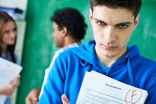 Sad student holding final exam paper with bad grade on it