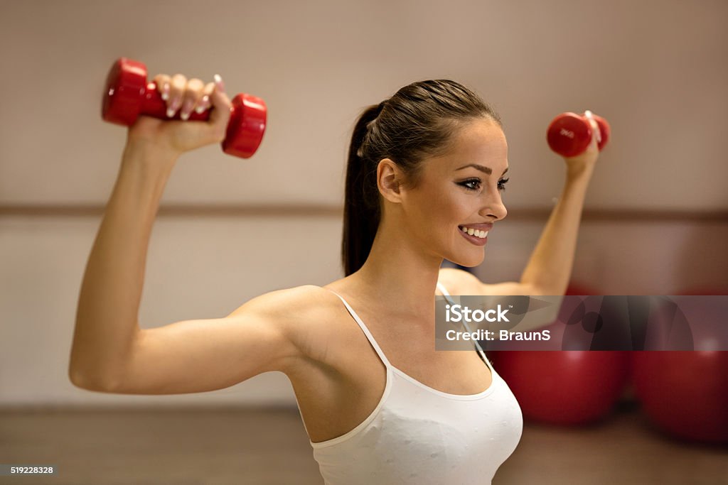 Happy woman exercising with dumbbells on a sports training. Young female athlete exercising with hands weights in a health club. Active Lifestyle Stock Photo