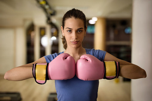 Young athletic woman having a boxing training in a gym and looking at the camera.