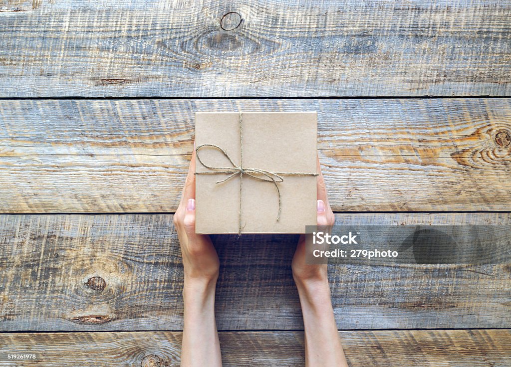 Womans hand holding craft gift box on wooden table Womans hand holding craft gift box on wooden table close up Gift Stock Photo