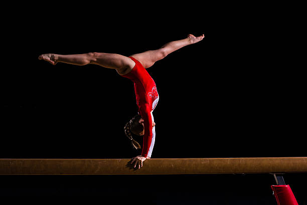 Female gymnast in sports hall Young woman balancing on balance beam in sports hall. gymnastics stock pictures, royalty-free photos & images