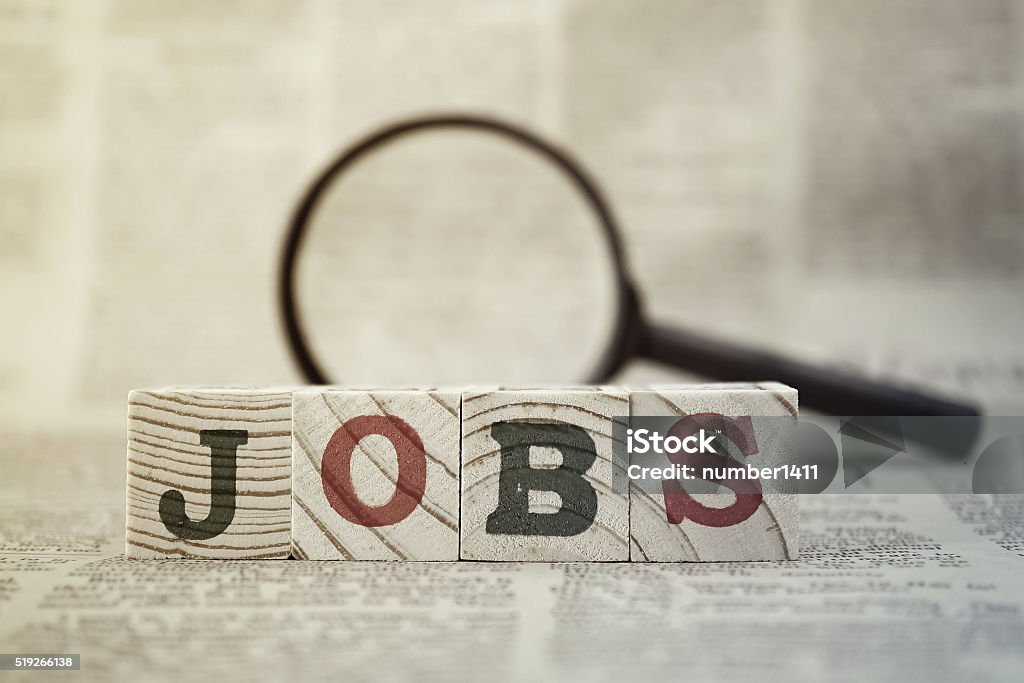 "Jobs" on wooden block and magnifying glass on newspaper background Occupation Stock Photo