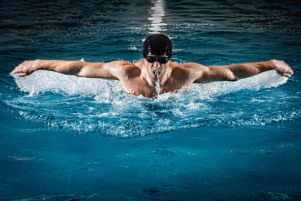 muskuläre junger mann schwimmen im schmetterling - breaststroke stock-fotos und bilder