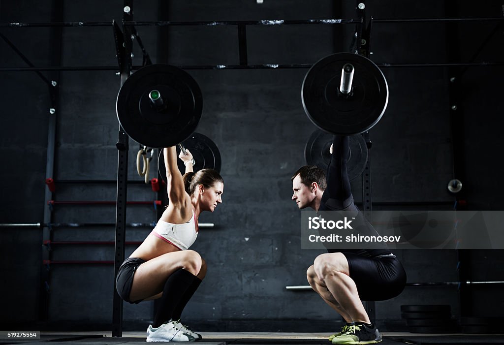 Weightlifting champions Active young man and woman lifting heavy barbells opposite one another Cross Training Stock Photo