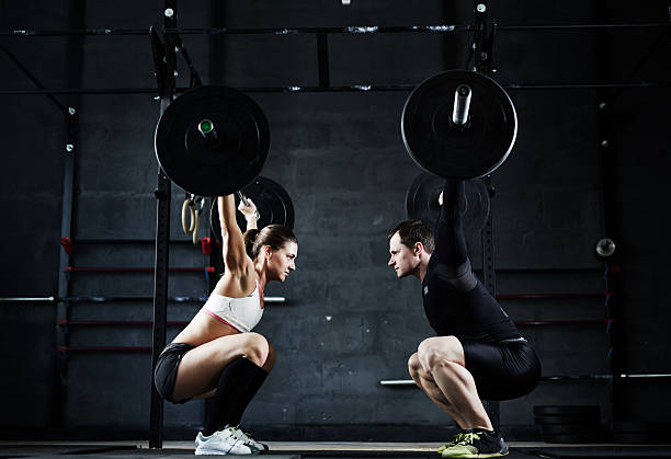 Weightlifting champions Active young man and woman lifting heavy barbells opposite one another cross training stock pictures, royalty-free photos & images