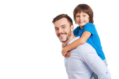 Side view of happy father carrying his son on back and smiling while both standing isolated on white