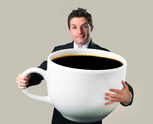 heureux homme d'affaires tenant drôle immense grande tasse de café noir machine a cafe/the - trop grand photos et images de collection