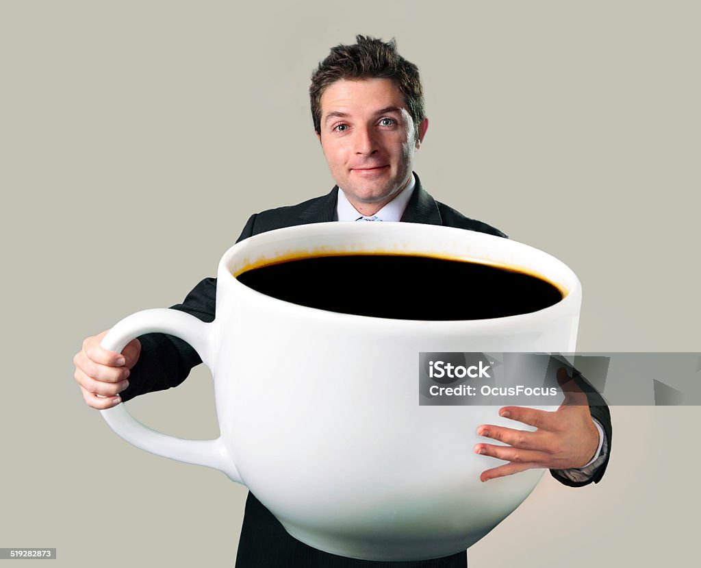 happy businessman holding funny huge  oversized cup of black cof young happy business man holding a funny huge and oversized cup of black coffee in caffeine addiction concept isolated on even background Coffee - Drink Stock Photo