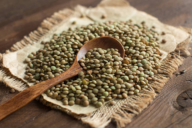 Green lentils with a spoon Green lentils with a spoon on a wooden table top view lentil photos stock pictures, royalty-free photos & images