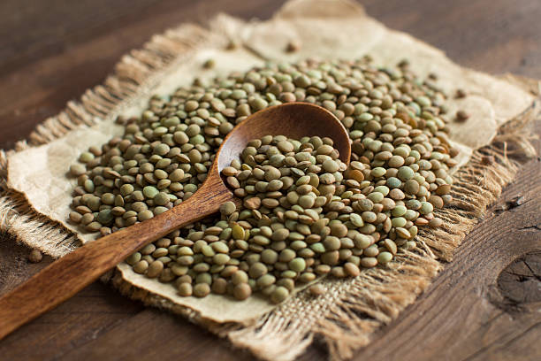 Green lentils with a spoon Green lentils with a spoon on a wooden table top view magnoliopsida stock pictures, royalty-free photos & images