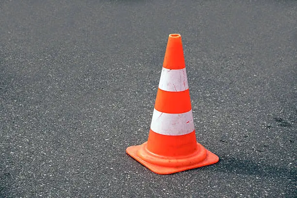 Photo of traffic cone, white and orange  on gray asphalt, copy space