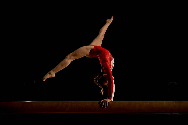 Female gymnast in sports hall Young woman stretching and balancing on balance beam in sports hall. gymnastics stock pictures, royalty-free photos & images