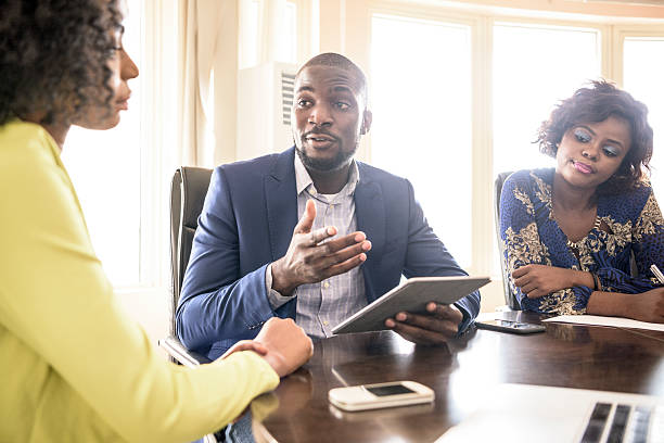 Businessman and two female colleagues in meeting Three young Nigerian business people in modern office having meeting, Nigeria, Africa. nigeria stock pictures, royalty-free photos & images