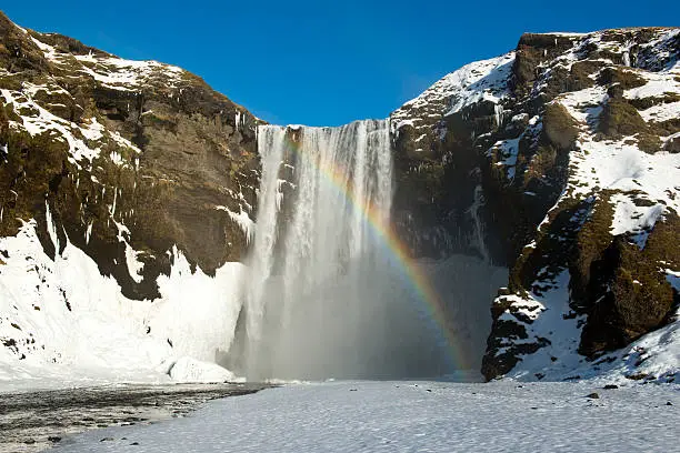 Photo of Winter Skogafoss waterfall with snow and rainbow, Iceland