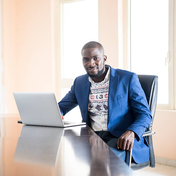 junge nigerianische geschäftsmann lächelnd in die kamera mit laptop - africa business aboriginal computer stock-fotos und bilder