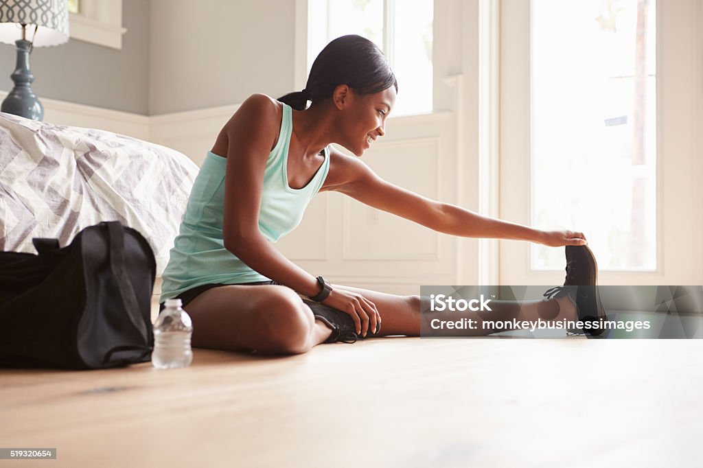 Young black woman sitting on the floor at home stretching One Woman Only Stock Photo