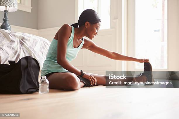 Young Black Woman Sitting On The Floor At Home Stretching Stock Photo - Download Image Now
