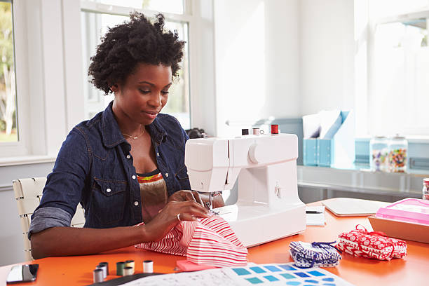 Young black woman stitching fabric using a sewing machine Young black woman stitching fabric using a sewing machine sewing machine stock pictures, royalty-free photos & images