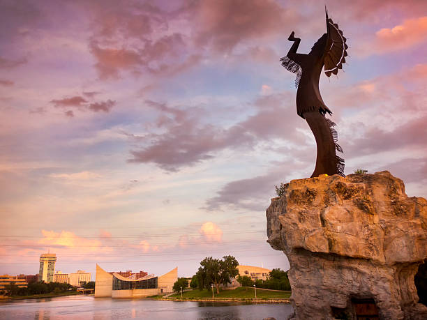 Beautiful Sunset With Keeper Of The Plains In Wichita Kansas A warm, beautiful sunset along the Arkansas River in Wichita, Kansas. The Keeper of the Plains in the foreground stands more than 70 feet tall including its promontory. kansas photos stock pictures, royalty-free photos & images