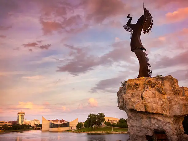A warm, beautiful sunset along the Arkansas River in Wichita, Kansas. The Keeper of the Plains in the foreground stands more than 70 feet tall including its promontory.