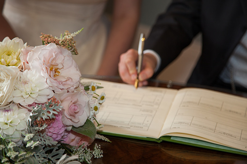 Signing the register at a wedding with a pen. The wedding bouquet is on tha table infront of the book