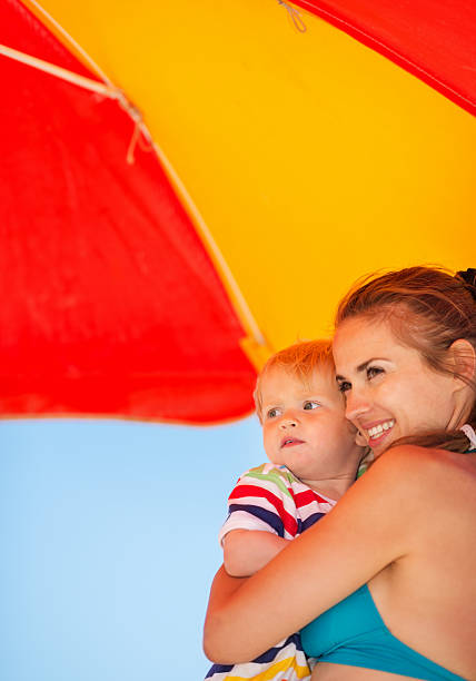 istock Mother and baby on beach under umbrella 519328621