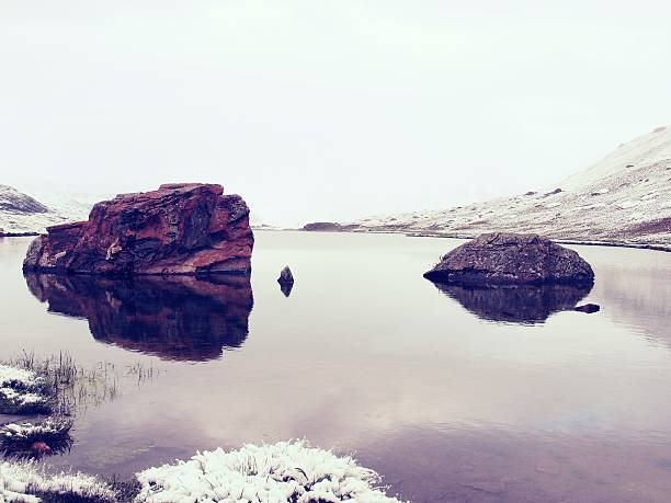 First snow in mountains. Autumn lake in Alps mirror level.