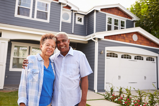 Senior black couple standing outside a large suburban house