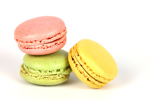 Studio shot of three French macaroons in yellow, green, and red colours on a white background. Pistachio, lemon, and strawberry taste.