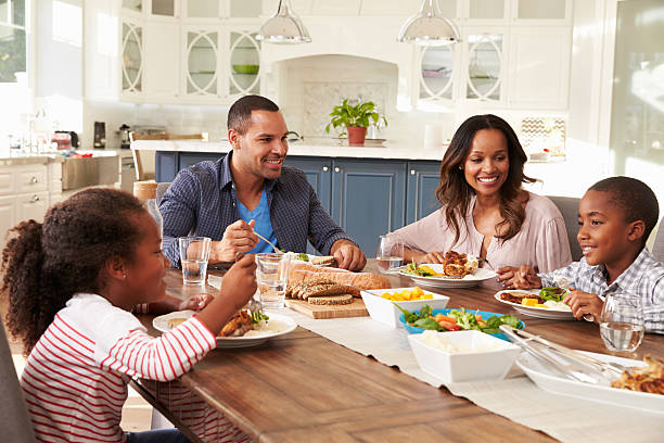 padres y de sus dos niños comiendo en la mesa de la cocina - mesa de comedor fotografías e imágenes de stock