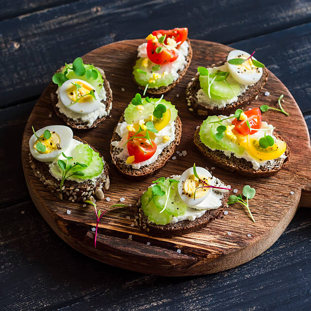 Sandwiches with soft cheese, quail eggs, cherry tomatoes and celery Sandwiches with soft cheese, quail eggs, cherry tomatoes and celery. Delicious healthy snack or Breakfast. On a wooden rustic board egg cherry tomato rye stock pictures, royalty-free photos & images