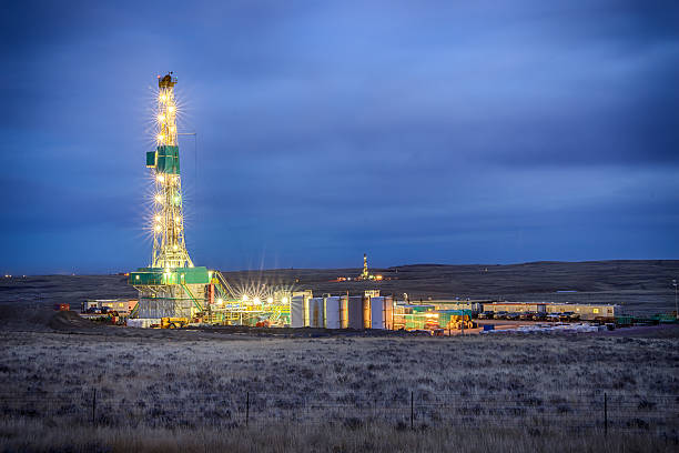 Drilling Fracking Rig at Night Evening shot of an oil Fracking Drill Rig with natural lens flaresFracking Oil Well is conducting a fracking procedure to release trapped crude oil and natural gas to be refined and used as energy wyoming stock pictures, royalty-free photos & images