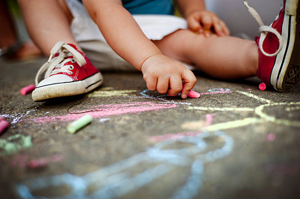 Close up of boy drawing with chalks Close up of little boy in canvas shoes drawing with chalks on the sidewalk chalk art equipment photos stock pictures, royalty-free photos & images