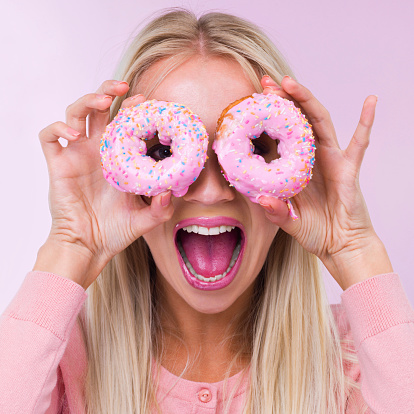Cropped shot of a woman holding donuts in front of her eyes while isolated on pink
